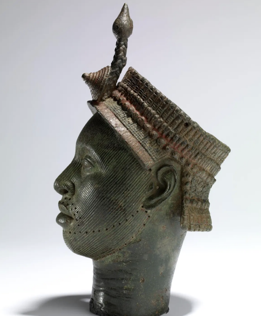 Brass Ife head in profile, wearing an ornamental headdress.