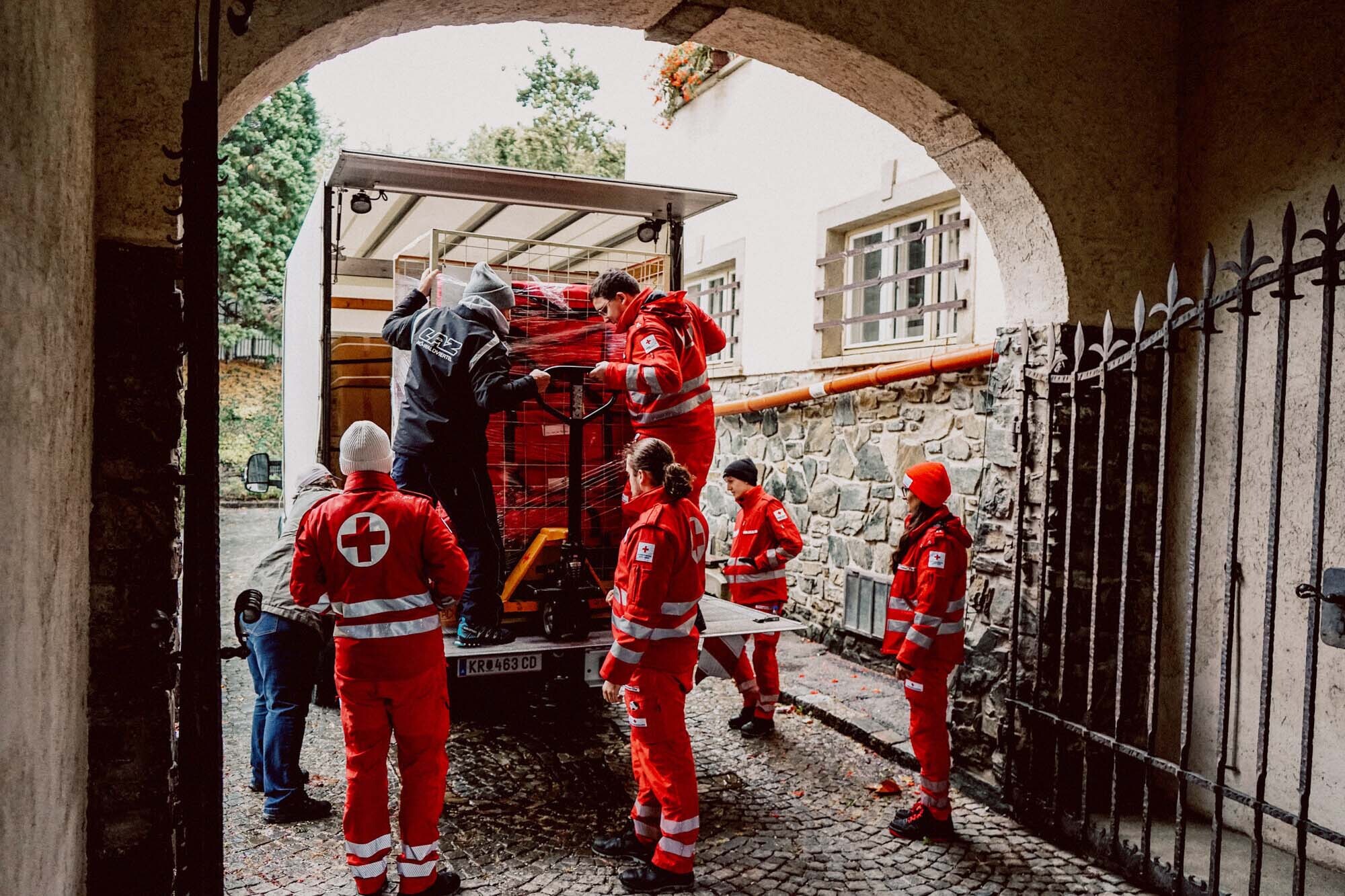 6 Mitarbeiter vom Roten Kreuz stehen hinter einem Rettungswagen. 