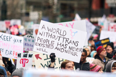 A pesron holding up a sign reading "A World Without Trans People Has Never Existed And Never Will" at a demonstration.