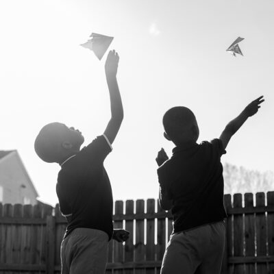 As the sun is shining, two children fly paper airplanes.