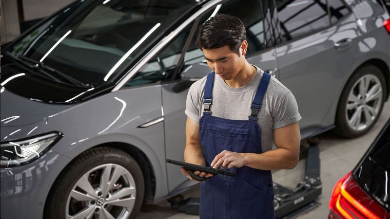 Ein VW Servicemitarbeiter lehnt an einer Wand der VW Werkstatt und hält ein Smartphone in der Hand