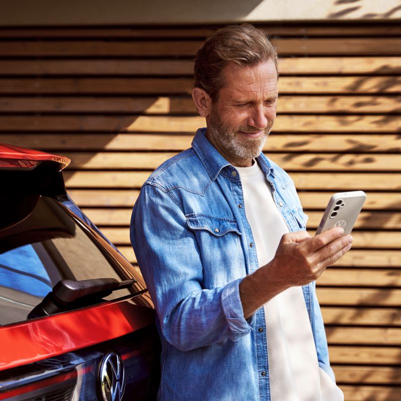 Mann schaut auf sein Handy vor seinem Volkswagen.