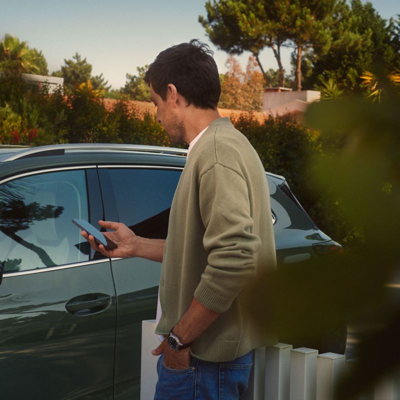 Person steht vor einem Volkswagen mit einem Mobiltelefon in der Hand