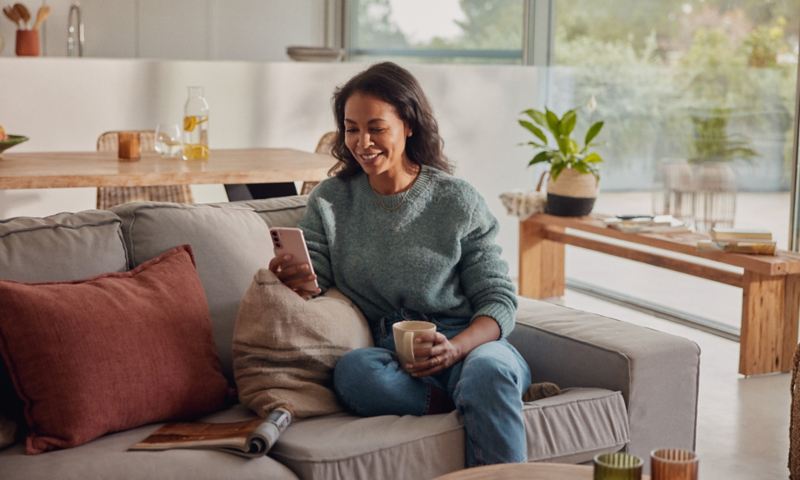 Eine Frau sitzt auf dem Sofa und schaut auf ihr Smartphone.