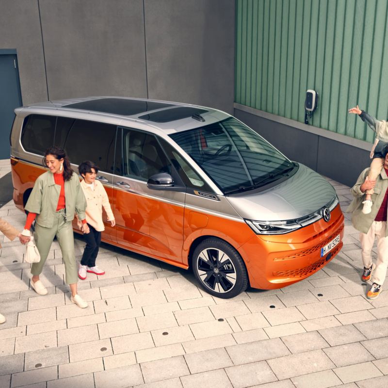 Der VW Multivan eHybrid parkt in einem Hof und eine Familie läuft um ihn herum.