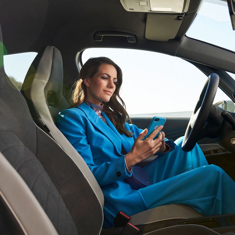 Eine Frau sitzt in einem Volkswagen und schaut auf ihr Handy