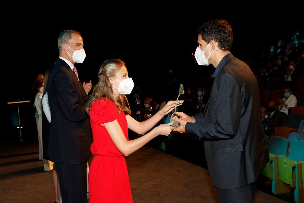 Dr. de la Fuente receiving a trophy from a woman in a red dress who’s standing beside others. All people pictured are wearing surgical masks as part of COVID-19 safety protocol.