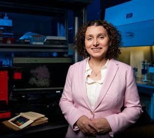 Dr. Eda Koculi standing in a lab with an old chemistry textbook lying open on the bench behind her.