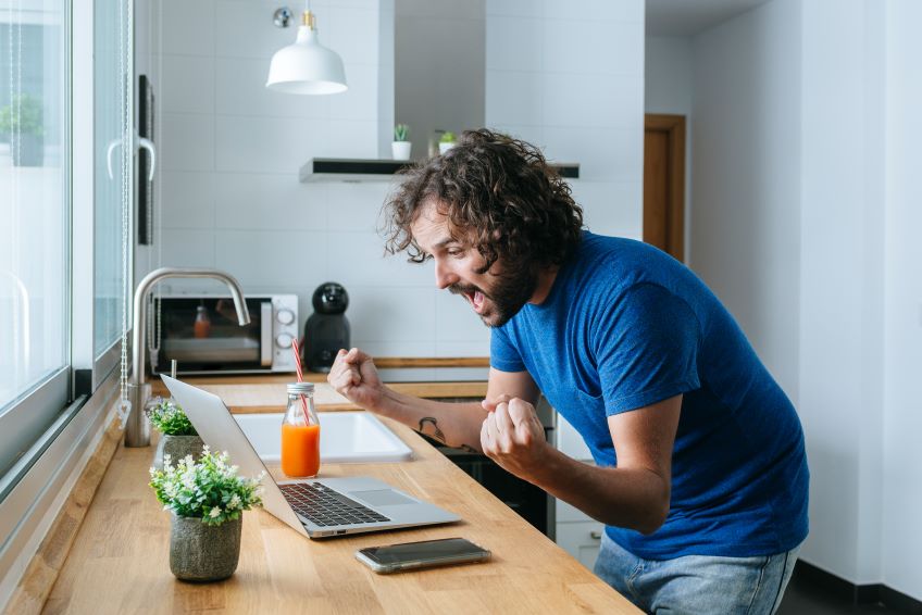 A fan watching the game on a laptop and cheering while standing at the kitchen counter