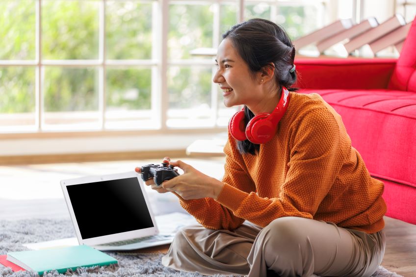 Individual sitting on the floor with a game controller in hand smiling at the screen