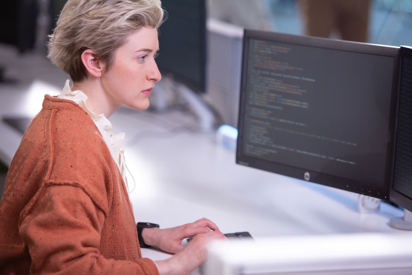 Businessperson sitting at a desk, looking at code on a monitor