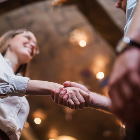 Due persone si stringono la mano in una stanza caldamente illuminata. La scena appare amichevole e professionale.