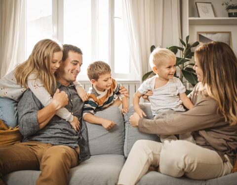 Un couple est assis sur le canapé de leur salon. Tous deux tiennent un enfant dans leurs bras et un petit garçon se tient entre eux.