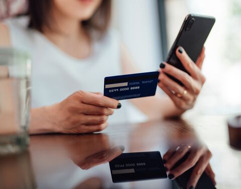 Una donna tiene una carta di credito in una mano e uno smartphone nell'altra mentre è seduta a un tavolo.