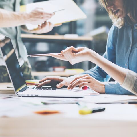 Due persone lavorano su un computer portatile mentre una di loro indica lo schermo con una penna per spiegare qualcosa.