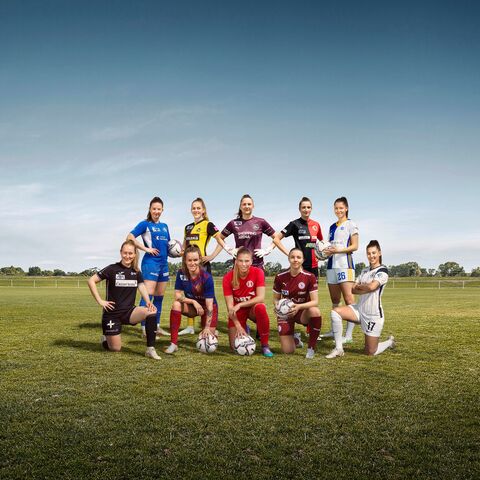 A group of nine female soccer players in different shirts pose on a soccer field, each holding a soccer ball.