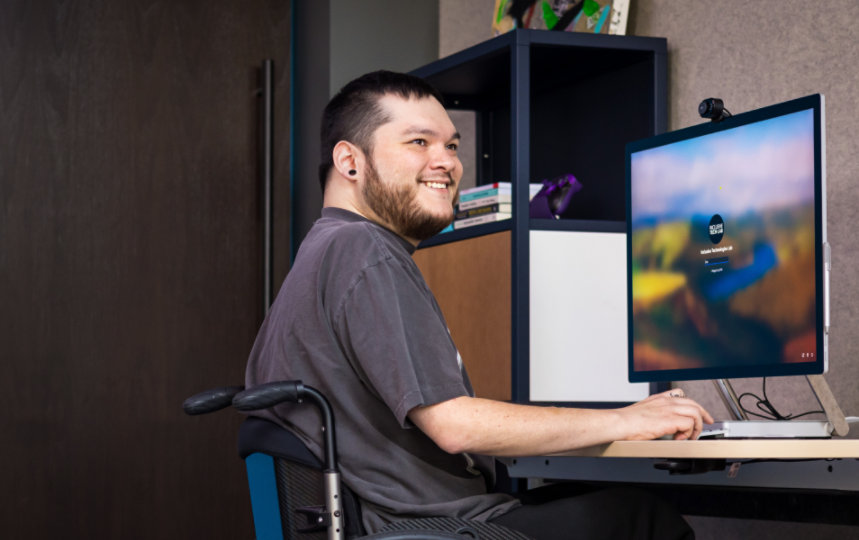 Une personne souriante en fauteuil roulant travaillant avec son PC de bureau.