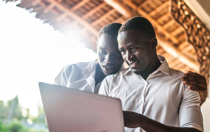 Two young men standing outside viewing a laptop. 