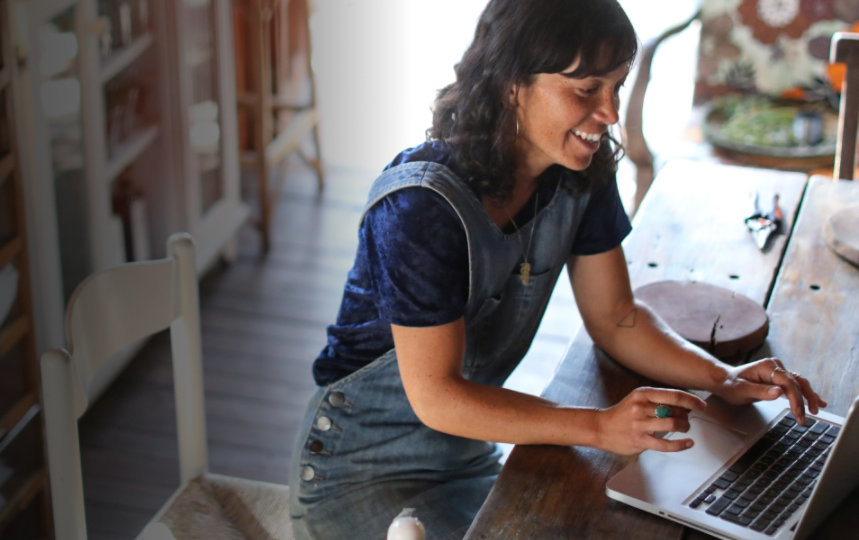 A casually-dressed woman works on a laptop at home.