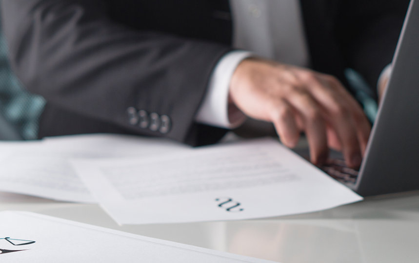 Closeup of an employee in a business suit typing on a laptop.