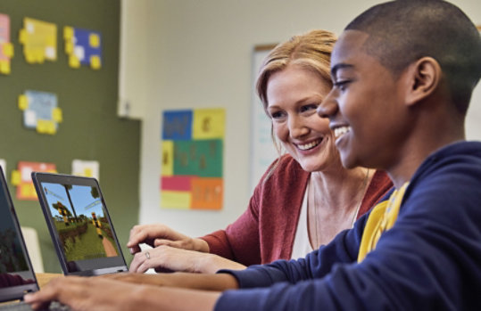 An adult and a young person smile while working on laptops.