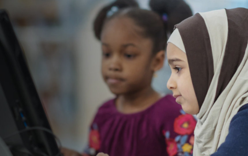 Two children look at a computer monitor.