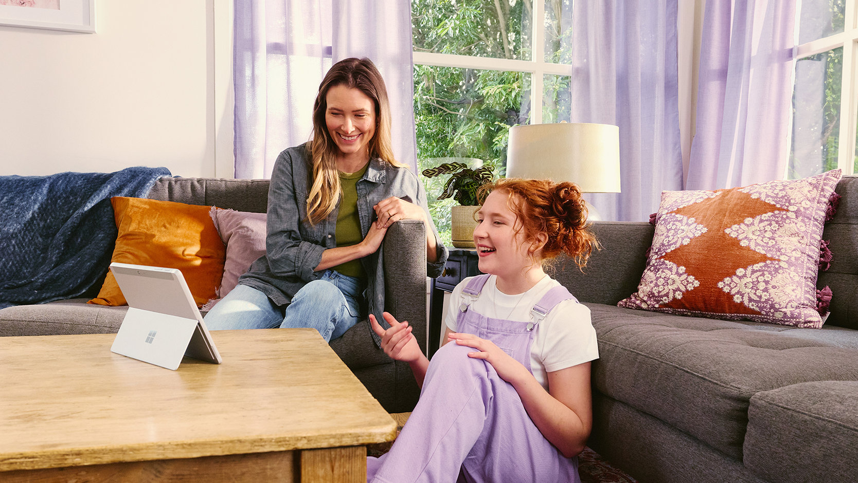 An adult and a young person sit in a living room using a tablet together.