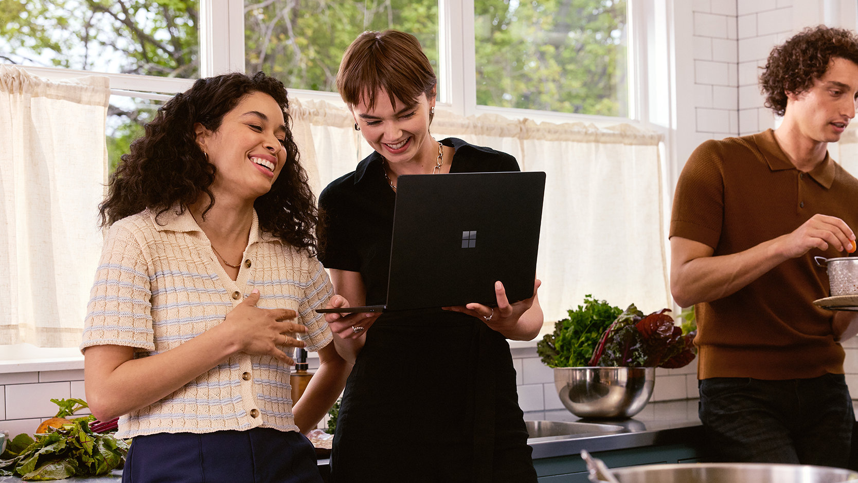 A group of friends use a laptop in a kitchen.