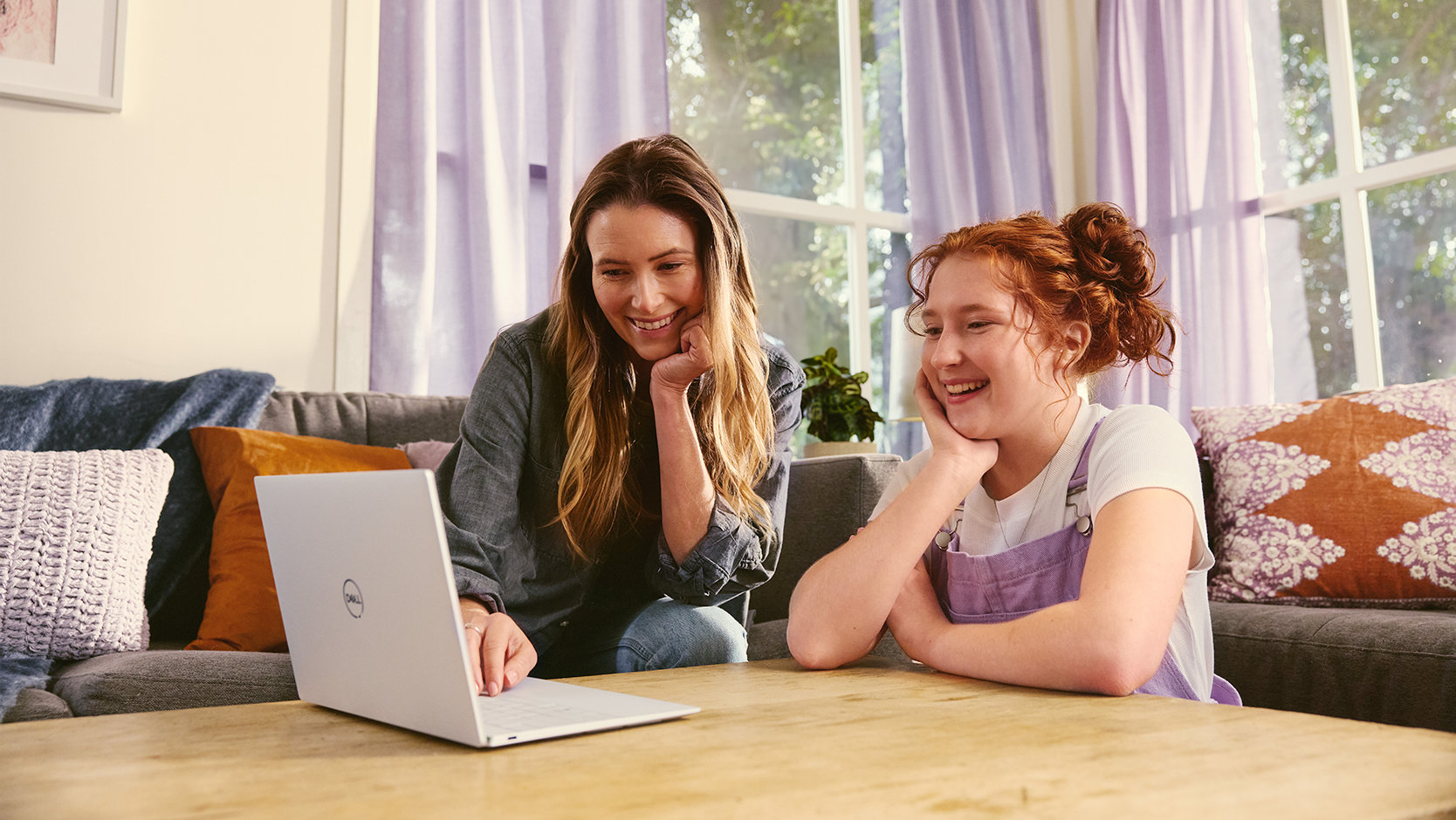 Ein Erwachsener und ein junger Mensch sitzen mit einem Laptop zusammen in einem Wohnzimmer.