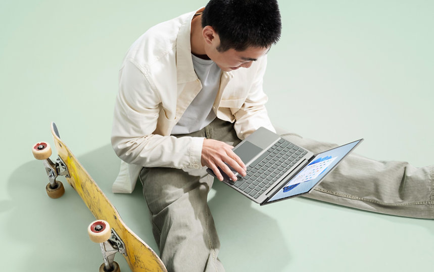 A student uses a Surface Laptop Go 2, while relaxing next to his skateboard.