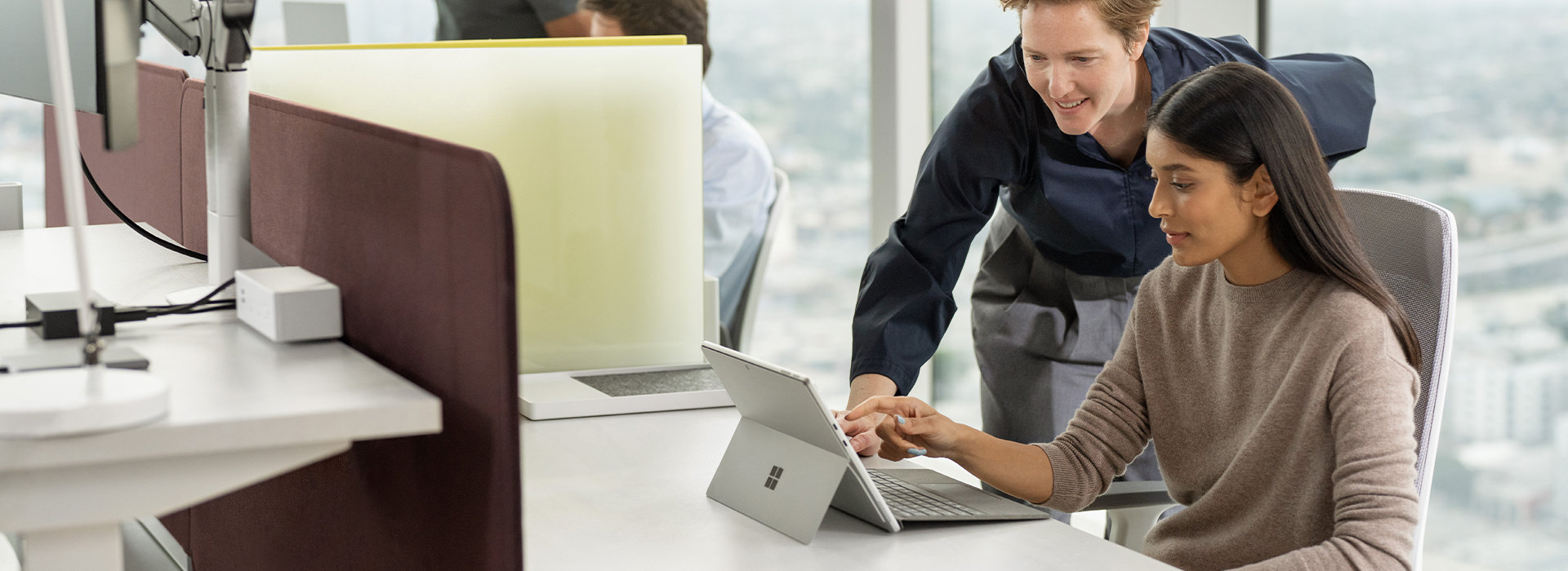 Une personne regarde par-dessus l’épaule d’une autre personne assise à un bureau et interagit avec l’écran d’un appareil Surface