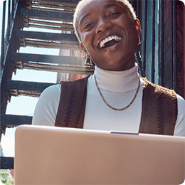 Person wearing a white shirt and brown vest, smiling, holding a PC