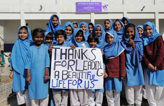 Un groupe d’enfants à l’extérieur tenant un panneau sur lequel est écrit « Thanks for leading a beautiful life for us » (« Merci de rendre notre vie plus belle »)