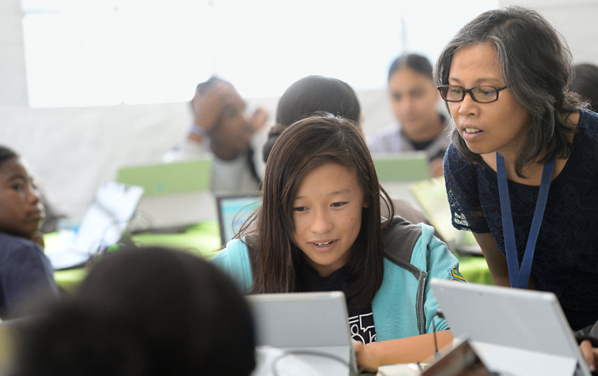 A teacher leans in to help a student working.