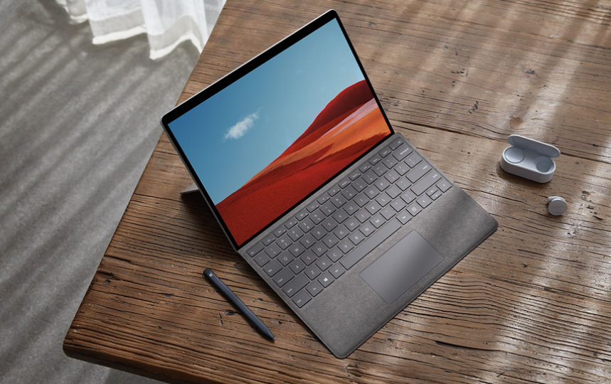 Surface Pro X on a desk with Surface Earbuds and a Surface Slim pen.