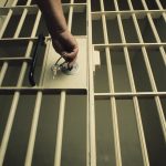 A person's hand inserting a key into the lock on a jail-cell door.