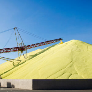 Image of a conveyor belt above two piles of yellow sulfur powder that appear to be tens of meters high.