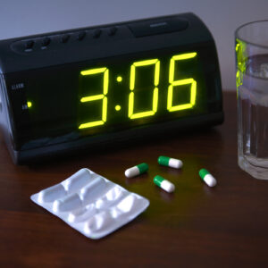 Sleeping pills on bedside table with clock and glass of water