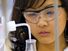 Close-up of a young female student (middle school, junior high school, laboratory) adding liquid with a dropper to a beaker of blue fluid (safety glasses).