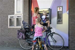 Een vrouw met twee kleine kinderen neemt geld op bij een pinautomaat