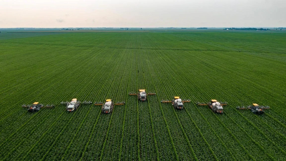 A series of agriculture vehicles in a vast green field.