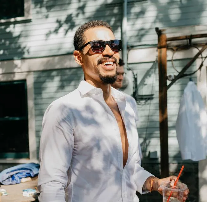 A man in a white shirt and sunglasses holding a drink.