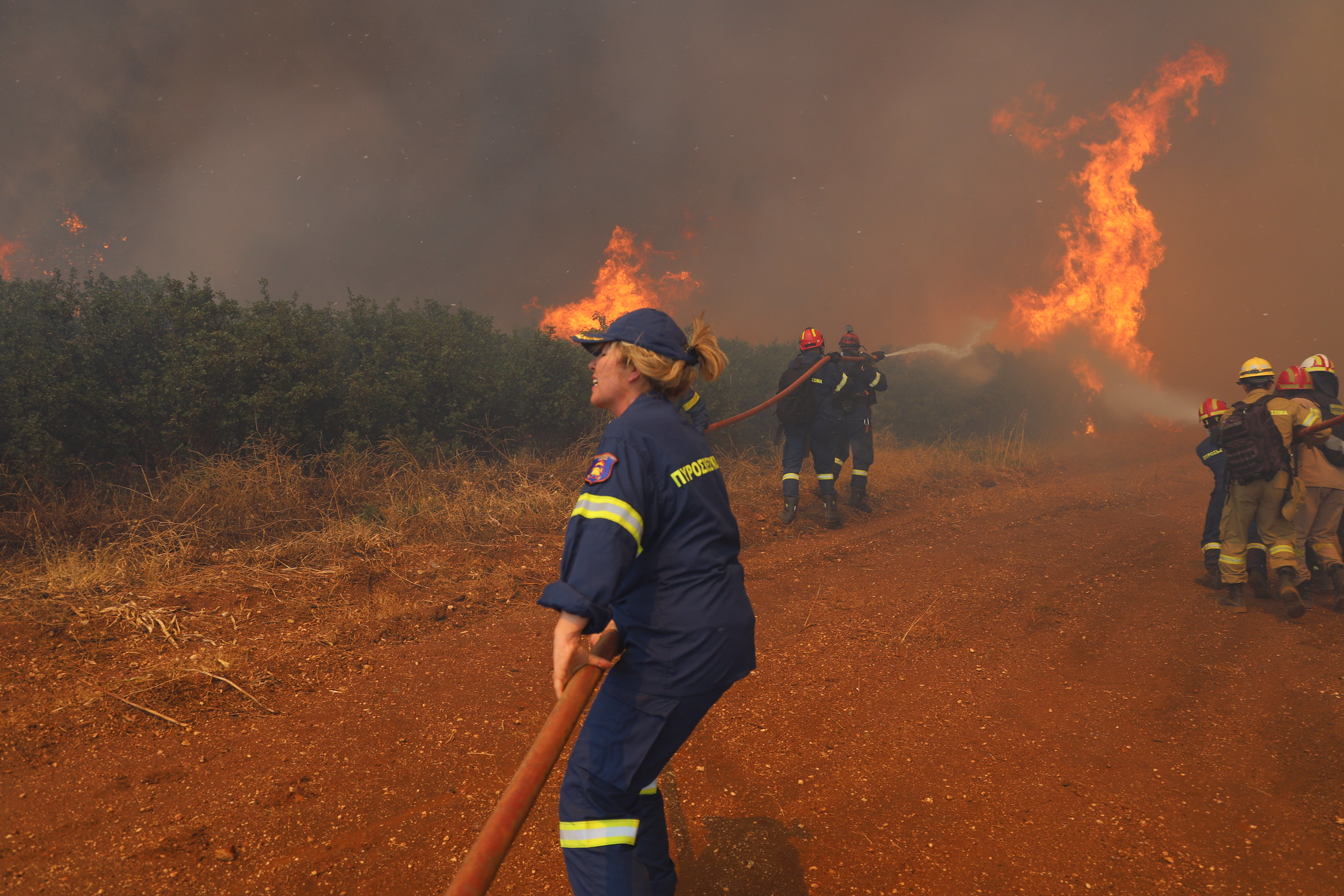 Fire fighter holding a hose, in the background a wildfire.