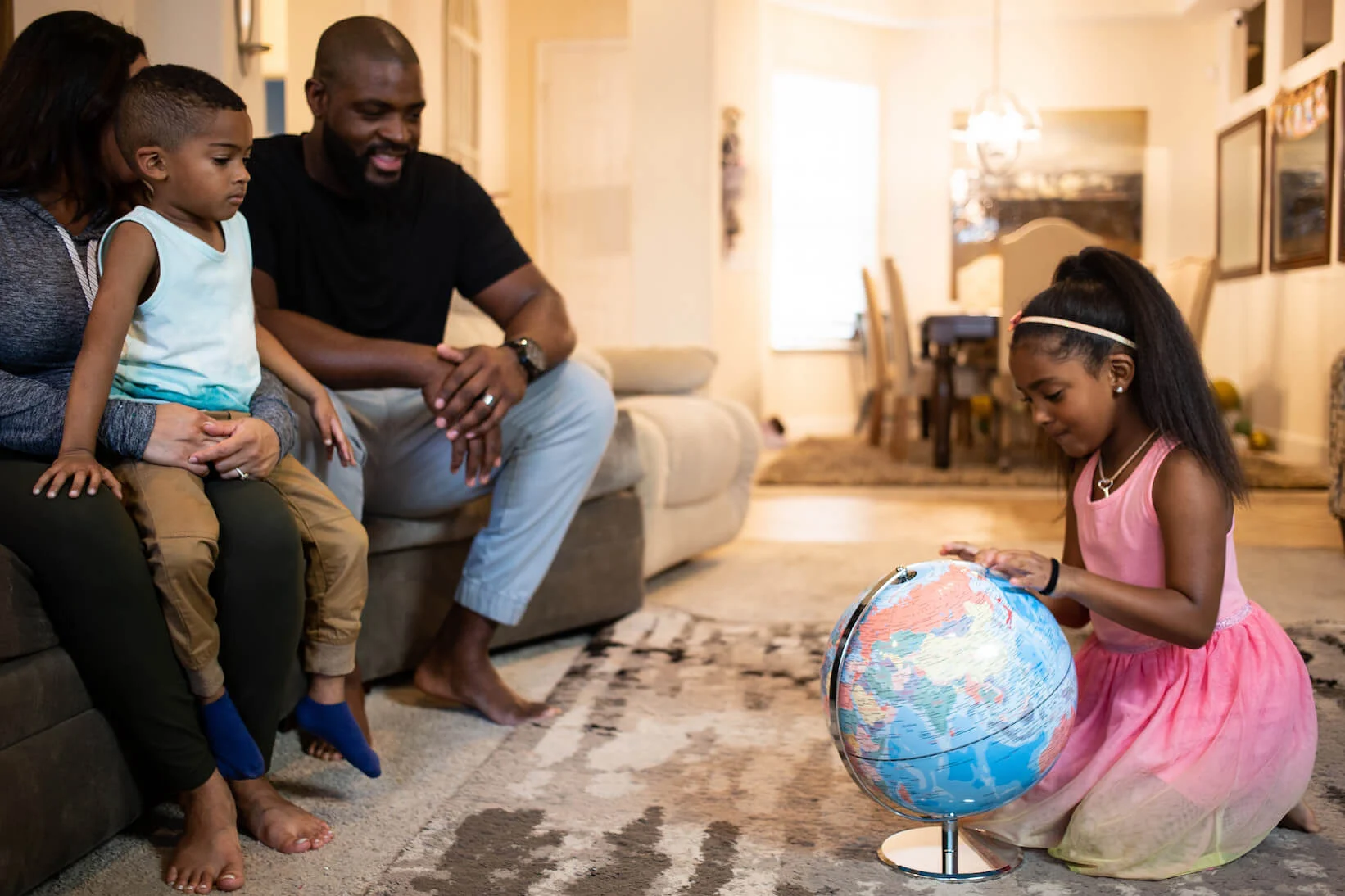 Family sitting on the couch watching as their daughter studies a globe.