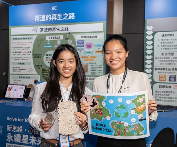 Two female students smiling by holding their projects