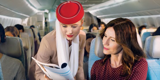 passenger and cabin crew member looking at a magazine together onboard Emirates Economy Class