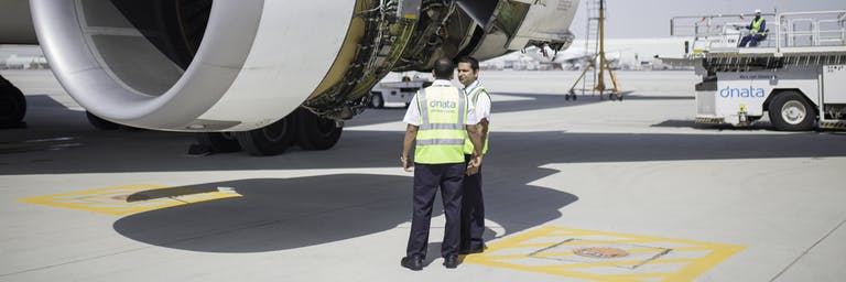 Dois funcionários de operações da dnata com roupa de alta visibilidade ao lado de um motor a jato