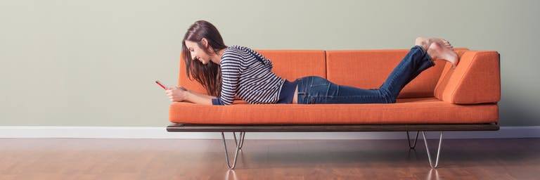 woman lying on orange sofa using a tablet to book a ticket