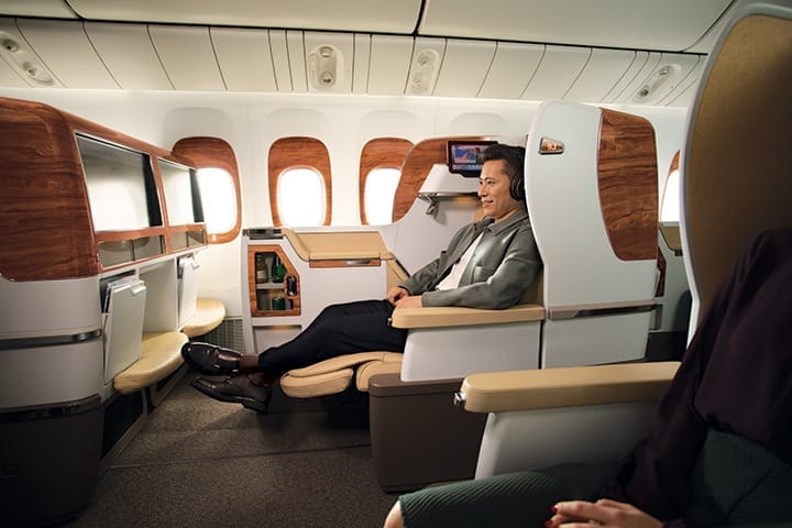 Een man met Business Class-hoofdtelefoon zit achterover in zijn stoel in Emirates Business Class en kijkt naar de breedbeeld-tv