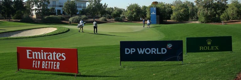 Golf course with Emirates sign and four people walking on grass